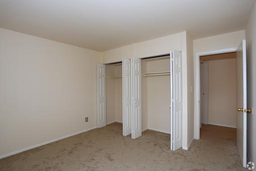 A room with white walls and a carpeted floor with a door on the right.