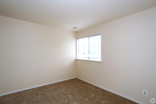 A room with a carpeted floor and a window letting in light.