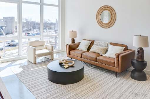 A living room with a brown couch, a white chair, and a round table with a yellow object on it.