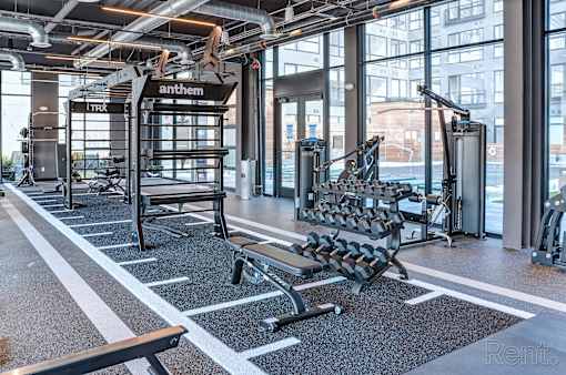 A gym with a variety of equipment including a bench, weights, and a TRX system.