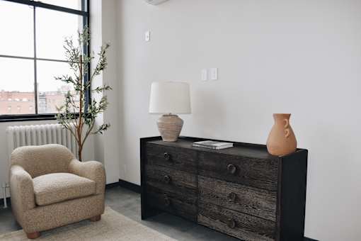 A room with a chair, a dresser, and a lamp.