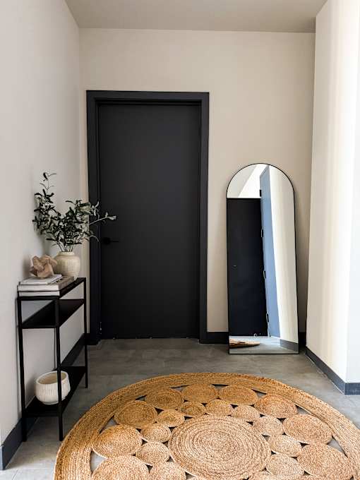 A black door is in a room with a round rug in front of it.