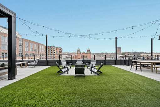 A rooftop patio with a green lawn and black chairs.