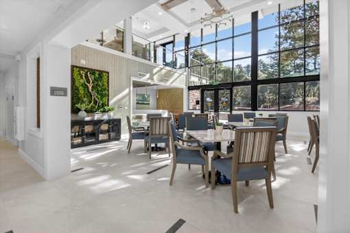 A modern dining room with a glass wall and a tree in the background.