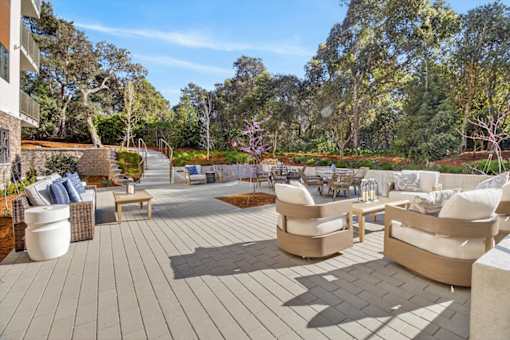 A patio with a grey floor and white furniture surrounded by trees.