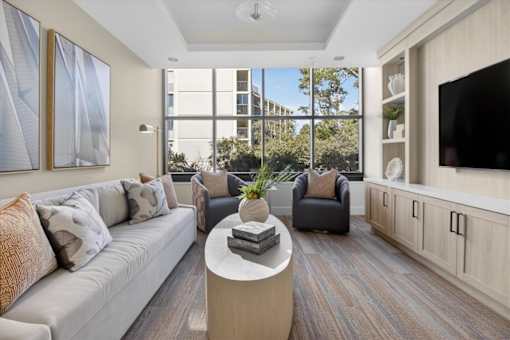 A living room with a grey couch, a coffee table, and a large window.