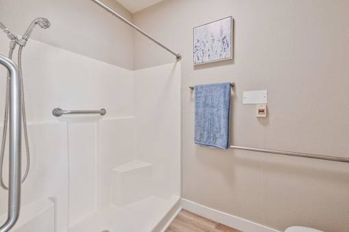 A white bathtub with a shower head and a blue towel hanging on the wall.
