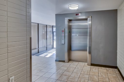 an elevator in a hallway with a tiled floor and stainless steel doors