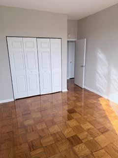 A room with a brown floor and white cupboards.