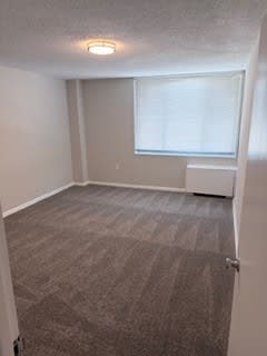 A room with a carpeted floor and a window with blinds.