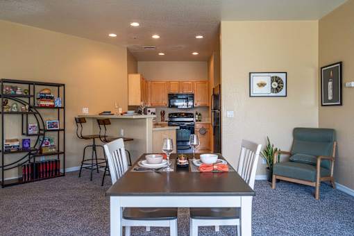 A dining room with a table set for two and a kitchen area in the background.