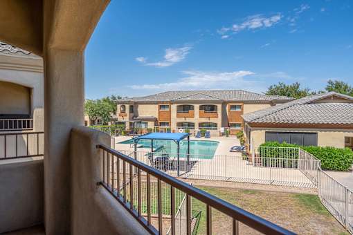 A view from a balcony looking out at a pool and a building.