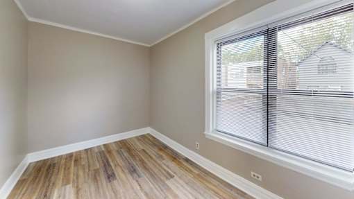 A room with wooden flooring and a window with blinds.