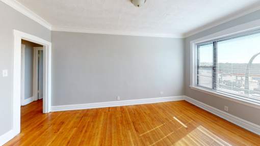 A room with wooden floors and a window overlooking a parking lot.
