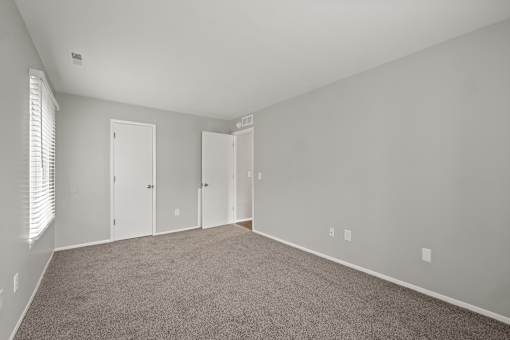 A room with carpeted floor and white walls with three doors.