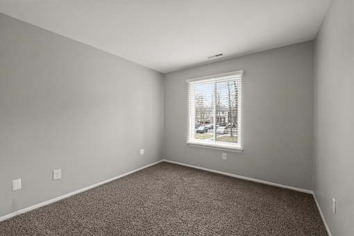 A room with a carpeted floor and a window showing a parking lot outside.