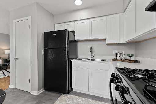 A black refrigerator in a kitchen with white cabinets.