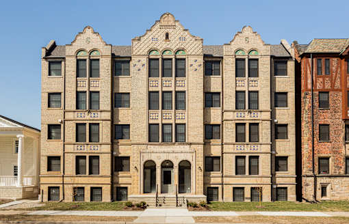 A large, beige, multi-story building with a balcony and arched doorways.