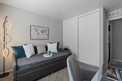 A modern bedroom with a grey bed, a grey chair, a white cabinet, and a framed world map on the wall.