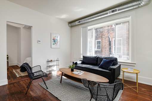 A living room with a black couch, a chair, a small table, and a window.