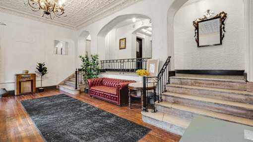 A red couch sits in the middle of a foyer with a staircase on the right.