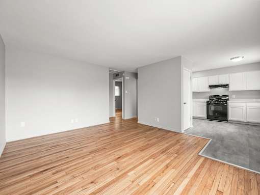 an empty living room with a hardwood floor and a kitchen in the background