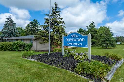 the entrance apartments sign in front of a lawn and trees