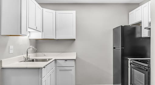 A kitchen with white cabinets and a black refrigerator.