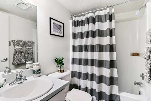 A bathroom with a striped shower curtain and a plant on the toilet.