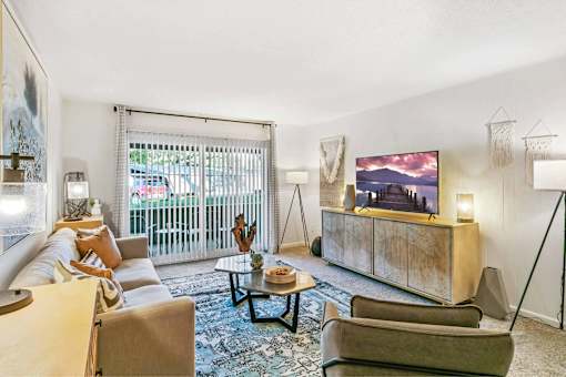A living room with a large screen TV and a view of a fence and trees outside.