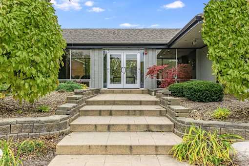 A building with a grey roof and a white door surrounded by green plants.