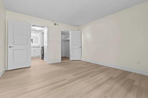 A room with white walls and wooden flooring with a door and a cabinet.