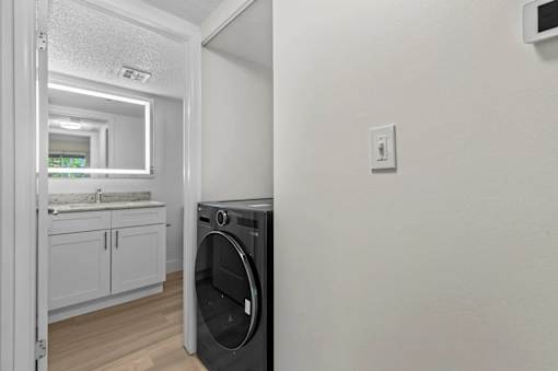 A washing machine is placed in a room with a white wall and a door leading to another room.