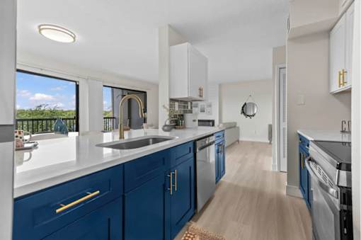 A kitchen with blue cabinets and a window overlooking a green landscape.