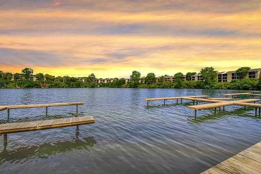 A serene lake with wooden benches and a building in the distance under a twilight sky.