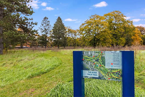 A sign for the River Walk Trail stands in a grassy field.