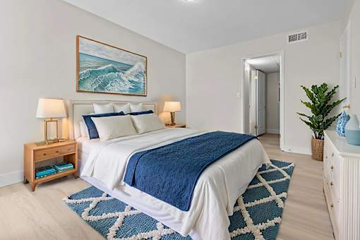 A bedroom with a large bed and a painting of a wave above it.