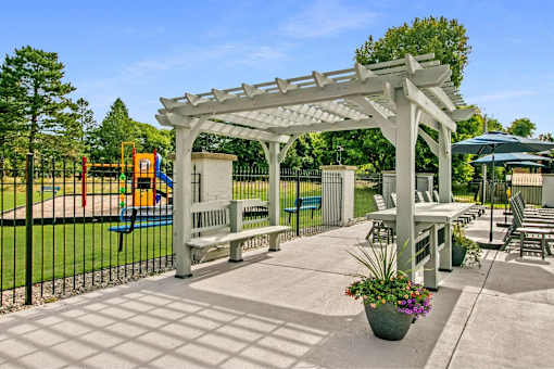 A white pergola is over a patio with a table and chairs.