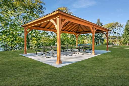 A wooden pavilion with a white base and a roof is surrounded by a grassy area.