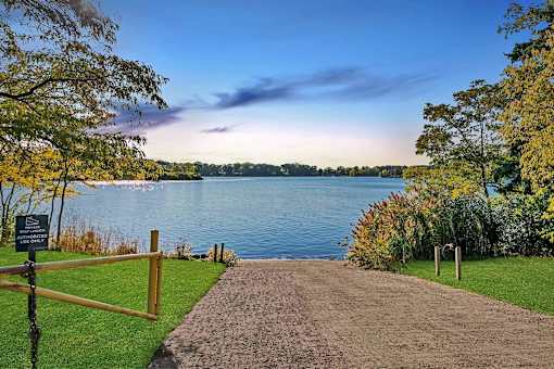 A pathway leads to a body of water with a sign on the left.