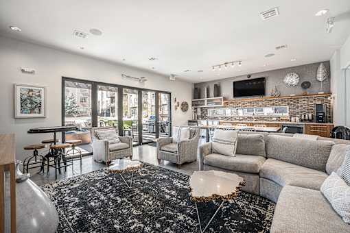 A modern living room with a black and white rug, a grey sofa, and a flat screen TV mounted on the wall.