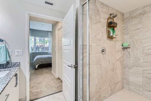 a bathroom with a shower and a bedroom in the background