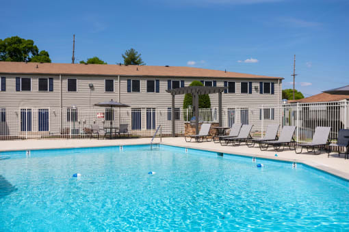 a large swimming pool with chairs and a building in the background