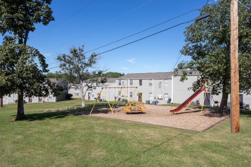 a playground with a swing set and a house in the background