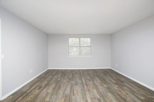 an empty room with wood floors and white walls and a window