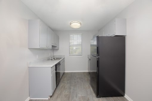 an empty kitchen with white cabinets and a black refrigerator