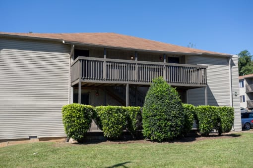 a house with a balcony and three bushes in front of it