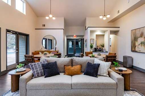 A living room with a grey couch and a round mirror on the wall.