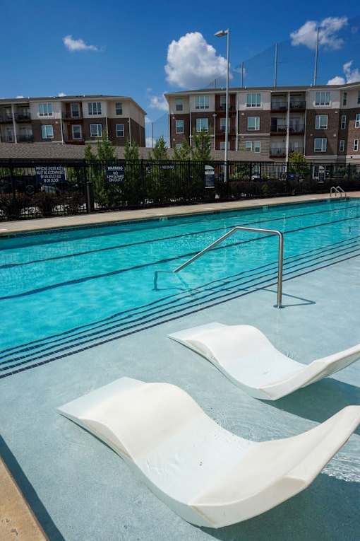 A swimming pool with white lounge chairs and apartment buildings in the background.