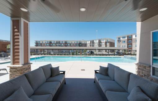 A large outdoor seating area with a pool and apartment buildings in the background at Woodstone at Metro North Crossing Apartments, Kansas City, Missouri